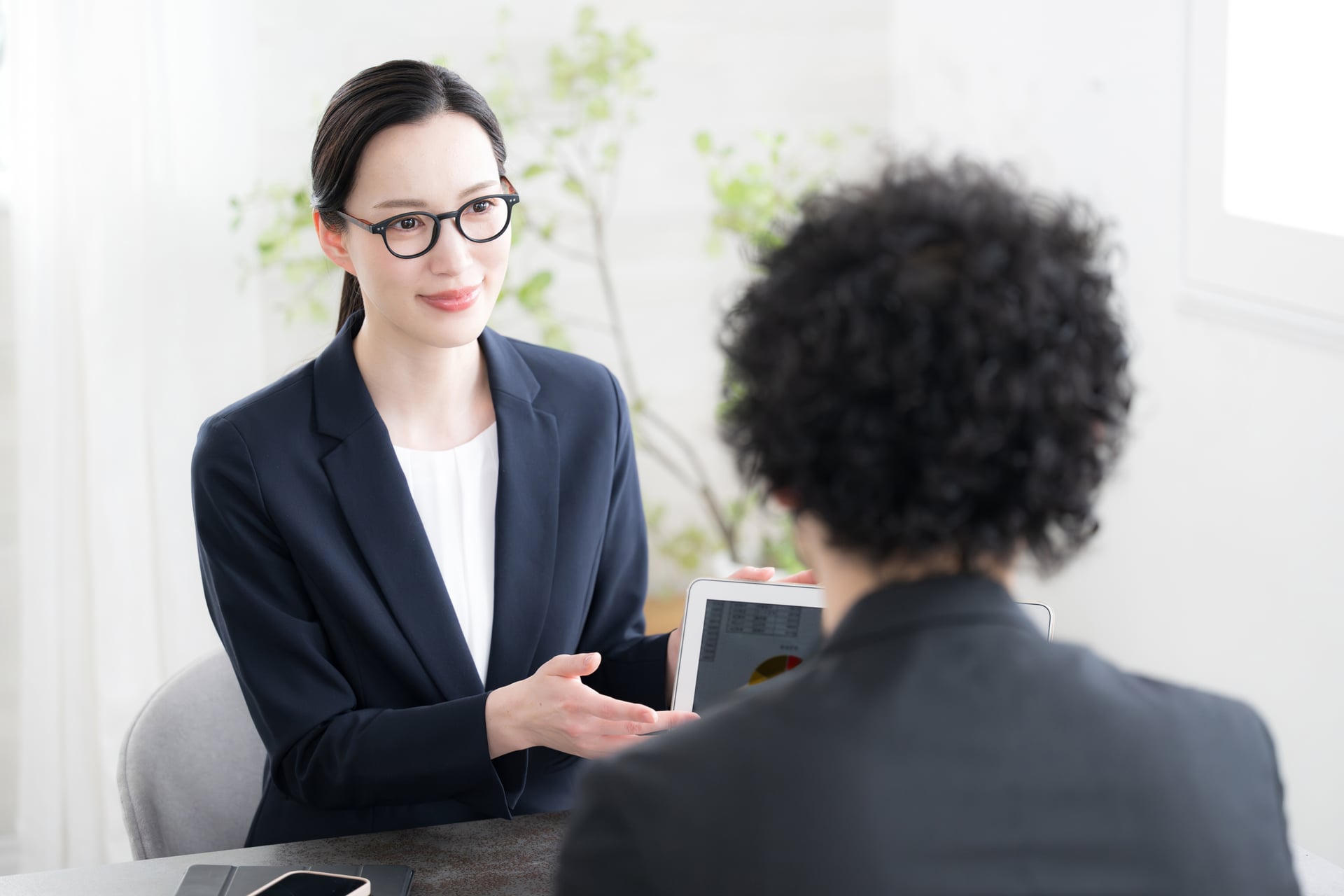 相談者に向き合い、パソコンを示しながら説明する担当者のイメージ